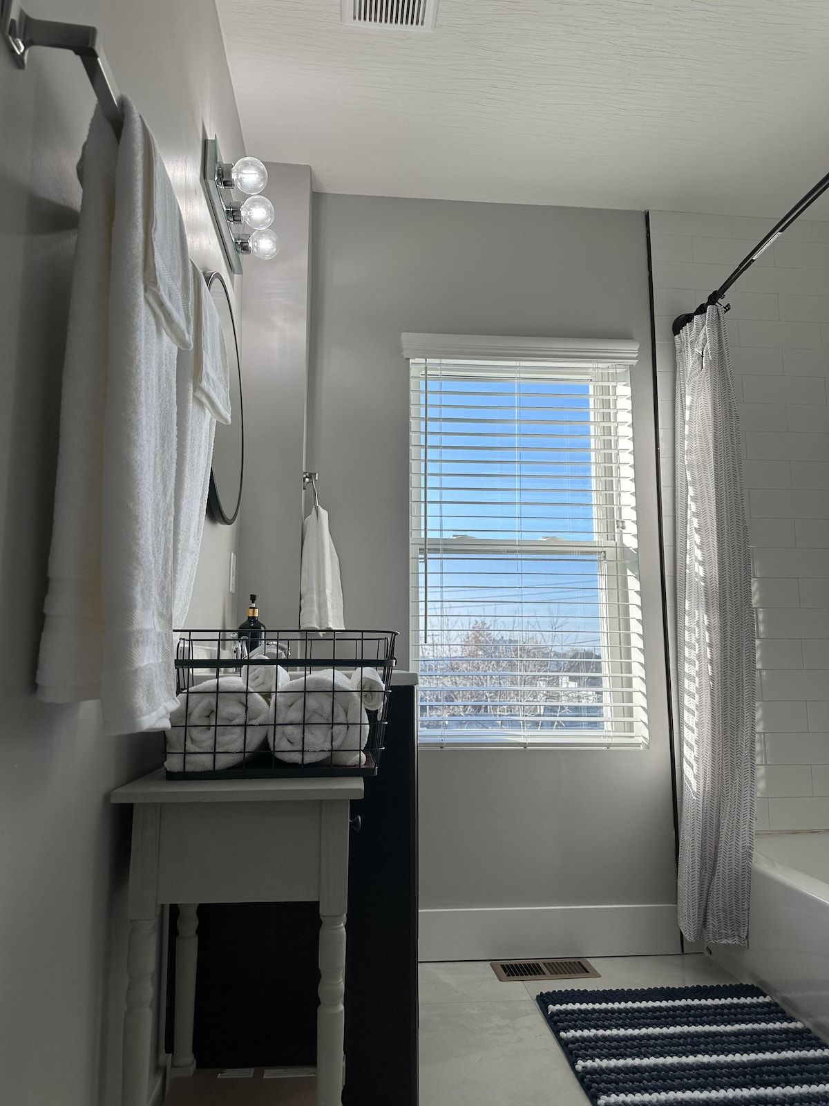 A bathroom with a window, a towel rack, a sink with a towel holder, and a shower curtain.