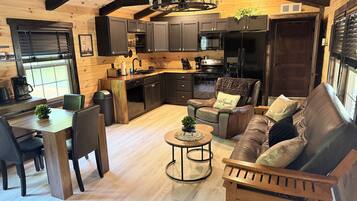 Un intérieur chaleureux comprenant un coin repas, un canapé, une table basse et une cuisine avec des meubles sombres et des poutres en bois.