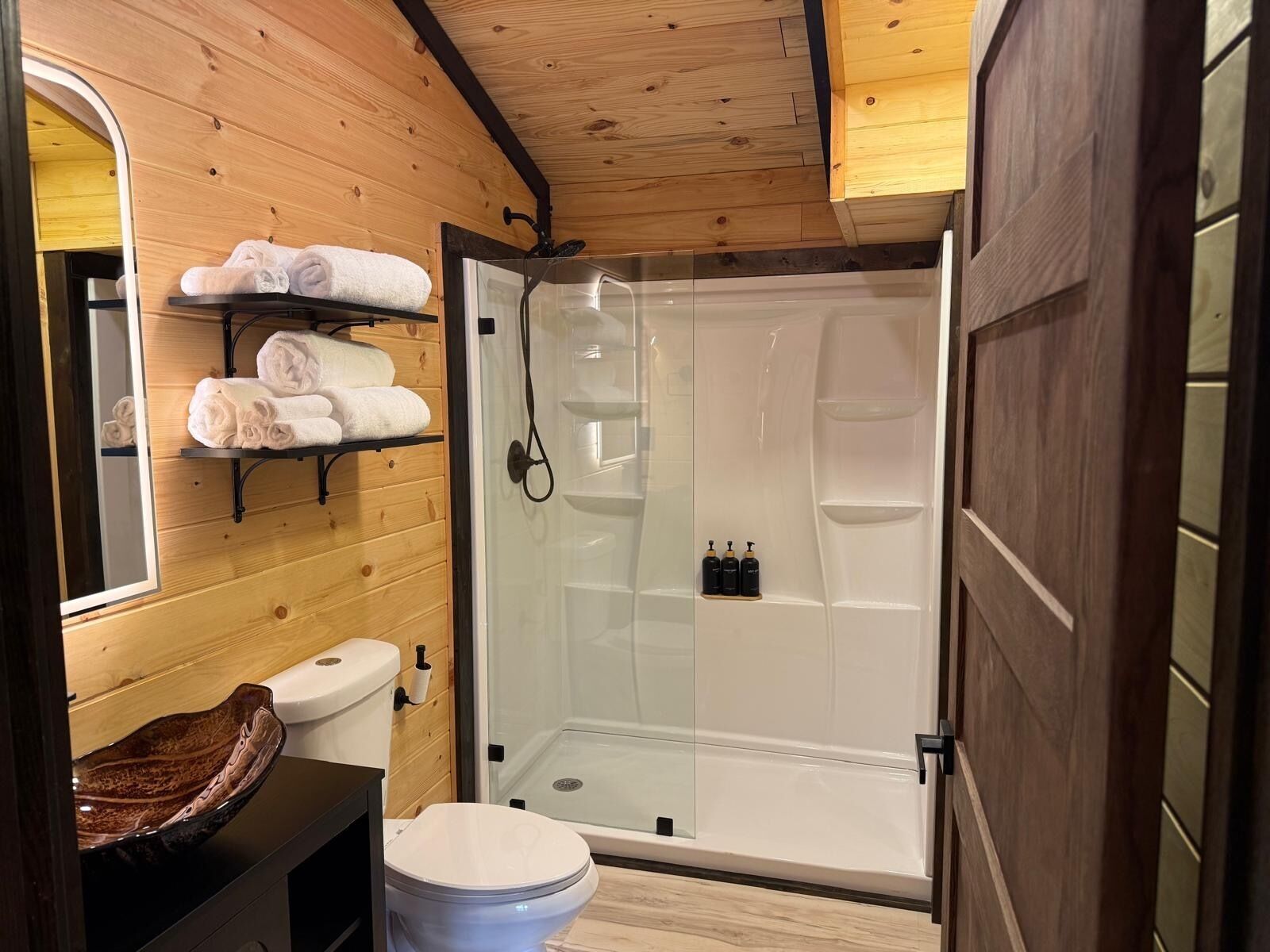 Une salle de bain compacte dotée d’une douche à parois de verre, de toilettes et d’un meuble-lavabo en bois avec un lavabo en cuvette.
