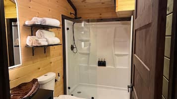 Une salle de bain compacte dotée d’une douche à parois de verre, de toilettes et d’un meuble-lavabo en bois avec un lavabo en cuvette.