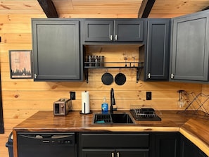Eine Küche mit dunklen Schränken, einer Holz Arbeitsplatte, einem Geschirrspüler, einem Weinkühlschrank und einem Bild an der Wand.