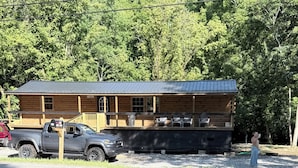 A cabin with a porch, a truck parked in front, and a person standing nearby.