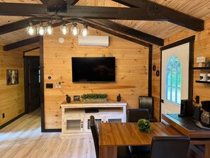 A wooden interior with a TV mounted on the wall, a dining area with a table and chairs, and a window with a view.