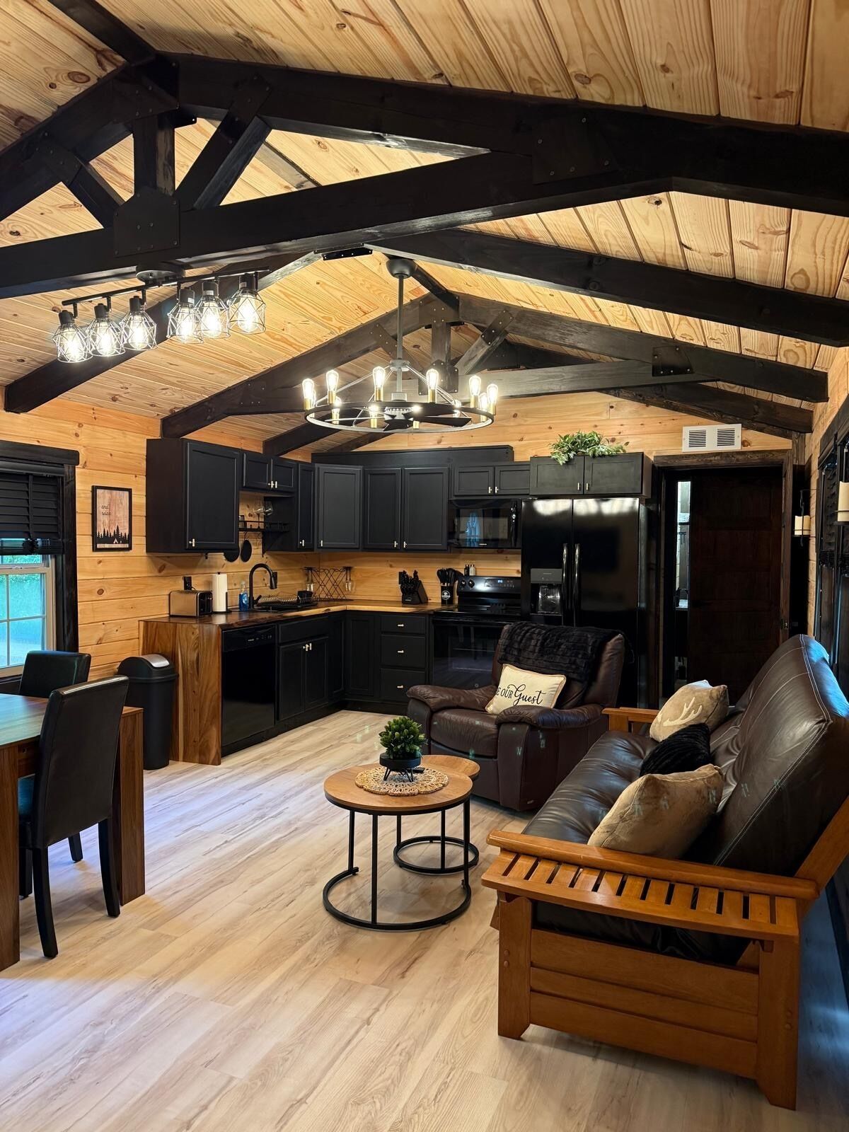 A spacious living area with a wooden ceiling, a dining table, a sofa, and a kitchen in the background.