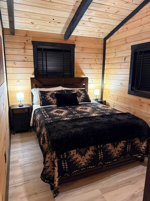 A wooden-paneled room with a bed, two bedside tables, and a window with shutters.