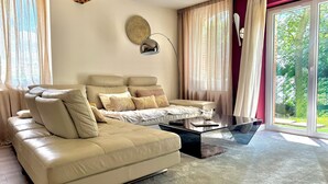 A living room with a sofa, a coffee table, and a view of greenery outside. - Apartment in a renovated farmhouse: 2 bedrooms · 40 m² terrace, garden, parking · 12 km from Toulouse (Lapeyrouse-Fossat)