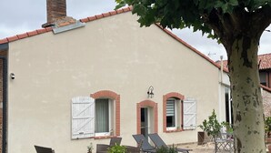 A house with a chimney, two windows with shutters, outdoor furniture, and a tree. - Apartment in a renovated farmhouse: 2 bedrooms · 40 m² terrace, garden, parking · 12 km from Toulouse (Lapeyrouse-Fossat)