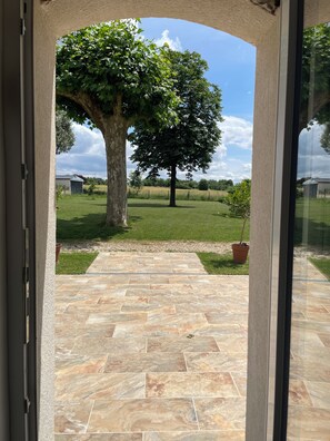 Un espace patio avec un sol en pierre menant à un champ herbeux et à un grand arbre.