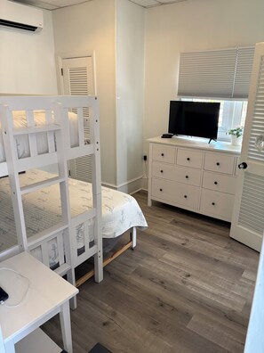 Un dormitorio con literas, un aparador con cajones, un televisor y una ventana con persianas.