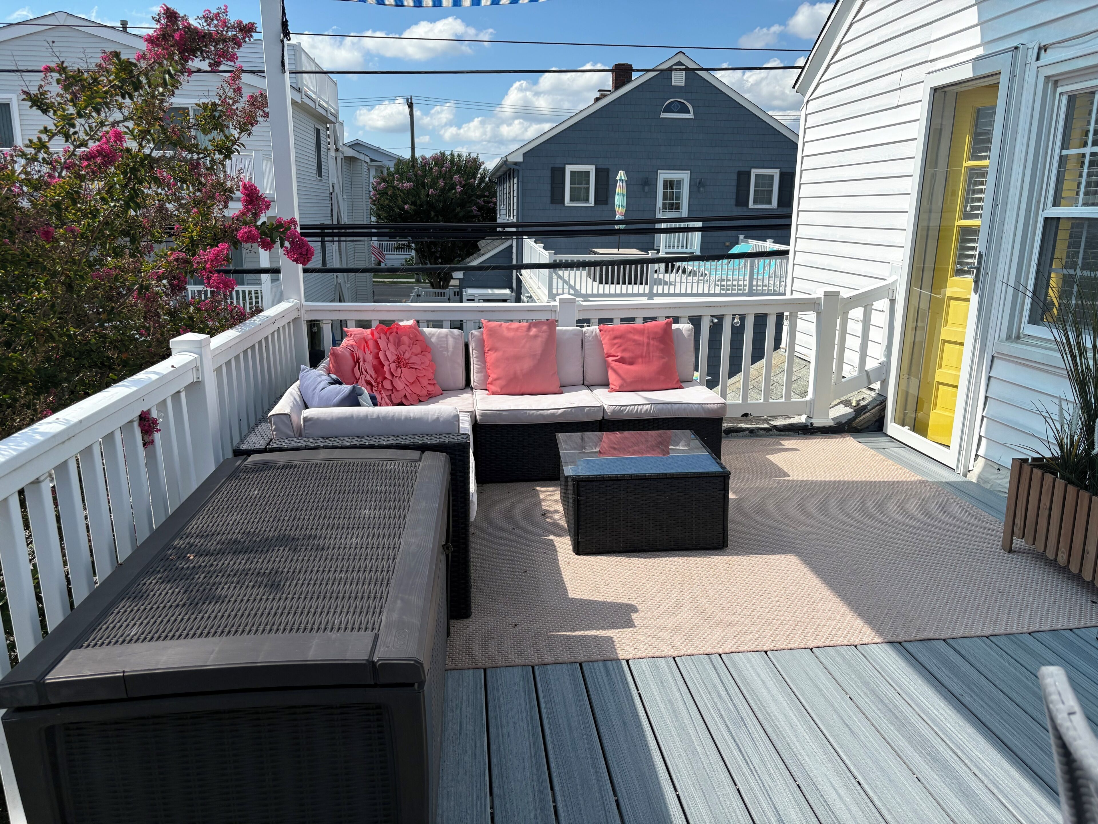 A covered outdoor deck with a sofa and a table, surrounded by a white railing.