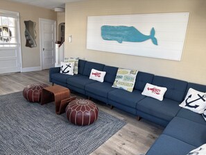 A living room with a blue sofa, nautical-themed cushions, a rug, and a whale artwork on the wall. - 5 Bedroom Beach House Steps to Beach and Boardwalk (Ocean City)