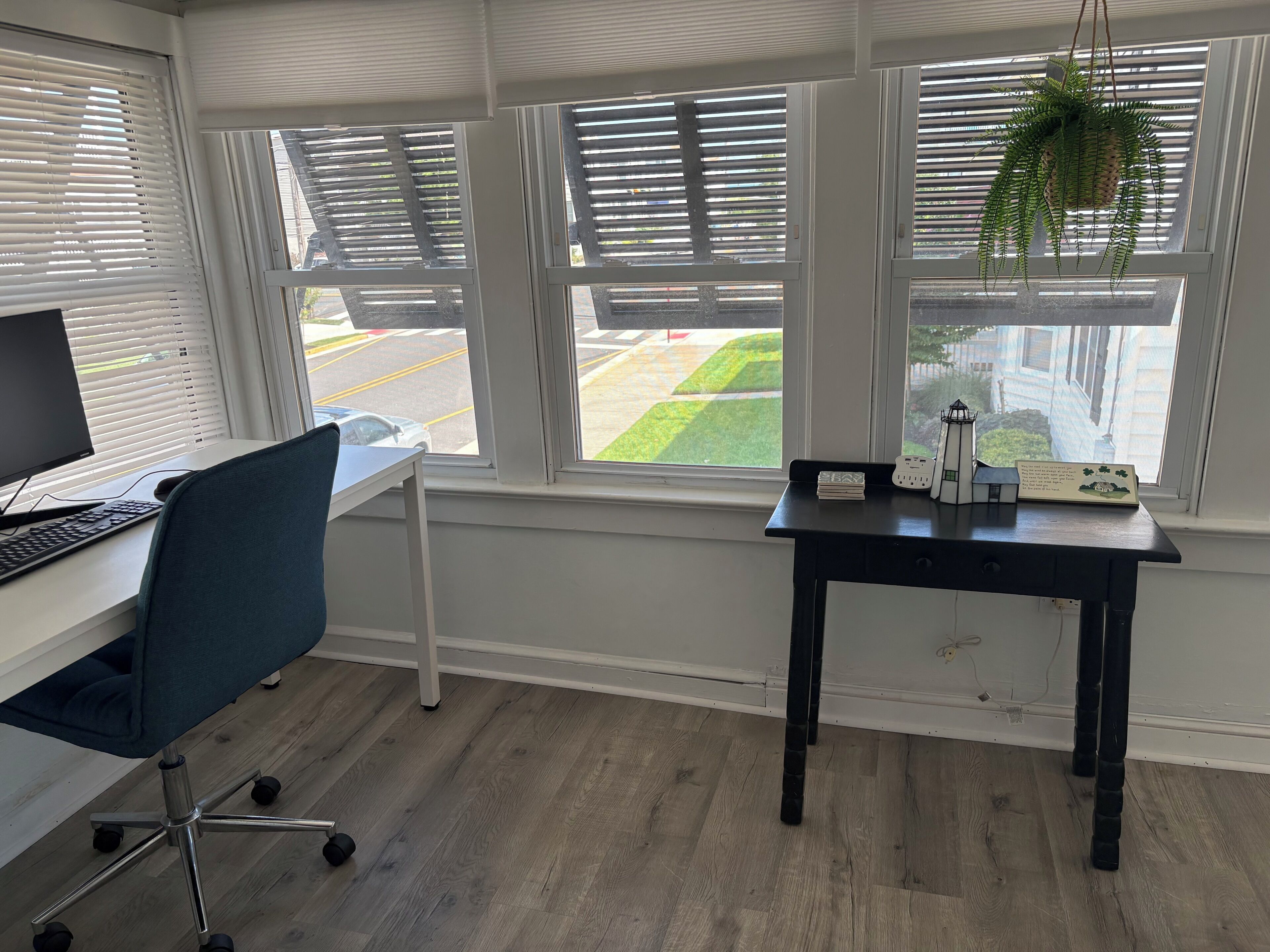 Ein Zimmer mit Schreibtisch, Computer, Stuhl und einem kleinen Tisch mit Pflanze und Schild.