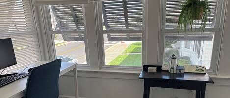 Une pièce comprenant un bureau, un ordinateur, une chaise et une petite table sur laquelle se trouvent une plante et un panneau.
