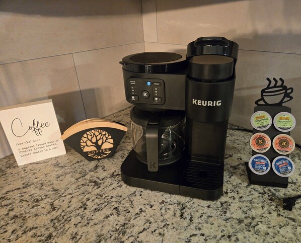 A Keurig coffee maker on a granite countertop with a coffee-themed card and a selection of Keurig pods. - Cozy Warsaw Stay Near Winona Lake & Trails (Warsaw)