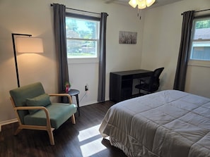 Un dormitorio con cama, escritorio, silla, lámpara y ventana.