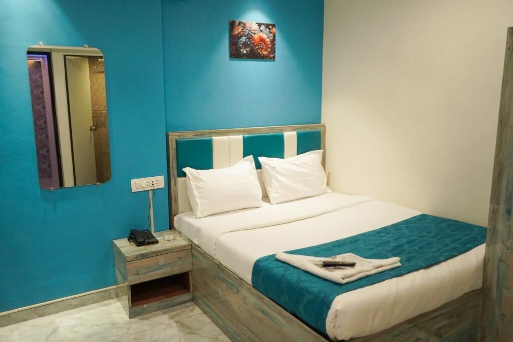 Una habitación de hotel con cama, mesita de noche, teléfono y espejo montado en la pared.