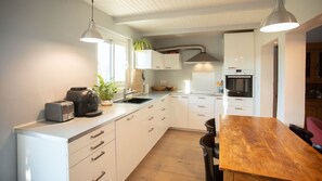 A modern kitchen with white cabinetry, a wooden dining table, and a built-in oven. - Piano in the Shadow of the Festival (La Roque-d'Anthéron)