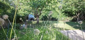 A garden with a tree, a blue structure, and various plants. - Piano in the Shadow of the Festival (La Roque-d'Anthéron)