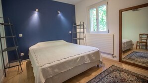 A bedroom with a bed, a window, a mirror, and a wooden floor. - Piano in the Shadow of the Festival (La Roque-d'Anthéron)