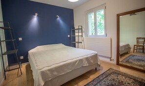 Ein Schlafzimmer mit einem Bett, einem Fenster, einem Spiegel und Holzboden.