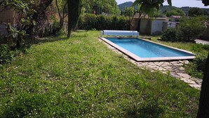 A rectangular swimming pool with a stone border, surrounded by a grassy area with various plants and trees. - Piano in the Shadow of the Festival (La Roque-d'Anthéron)