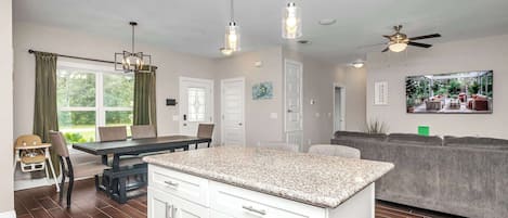 Una cocina moderna con armarios blancos, encimera de granito y comedor con mesa y sillas.