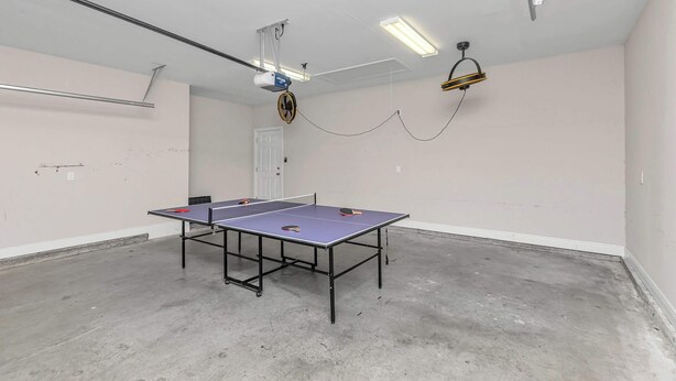 A ping pong table in a room with a ceiling fan, a projector, and a hanging light fixture. - Oyster Cove: Pets Allowed, Grill, Pong, Beach! (Navarre)