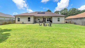A two-story house with a covered patio, a fenced yard, and a clear sky. - Oyster Cove: Pets Allowed, Grill, Pong, Beach! (Navarre)