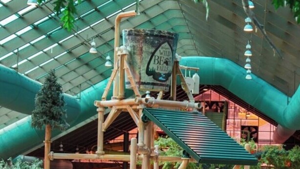 Un espace de jeux intérieur comprenant une structure d’escalade, des toboggans et une fresque murale.