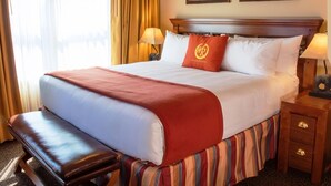 Une chambre d’hôtel avec un grand lit, une banquette, deux lampes de chevet et une table de chevet avec des tiroirs.