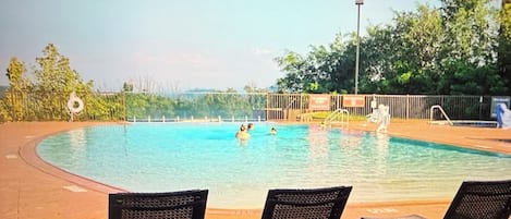 Ein Schwimmbecken mit drei Stühlen im Vordergrund und Blick aufs Wasser.