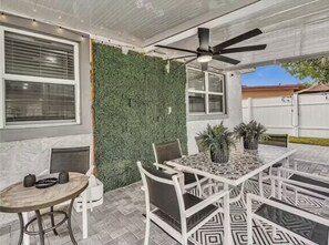 An outdoor patio area with a table and chairs, a ceiling fan, and a decorative wall. - Villa 2 Miles Beach 7 beds Sleeps 12 BBQ 5min Big Easy Casino & Aventura Mall (Hallandale Beach)