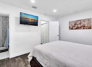 A bedroom with a bed, a TV mounted on the wall, a door, and a painting.