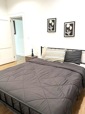 Une chambre à coucher comprenant un lit, une table de chevet, une lampe et deux tableaux accrochés au mur.
