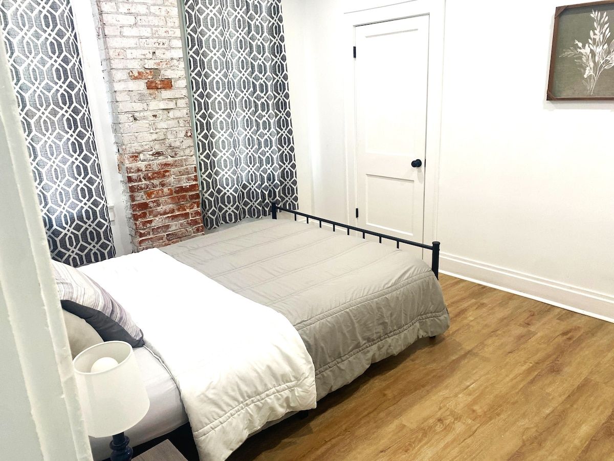 A single bed with a metal frame, a white door, and a patterned curtain.