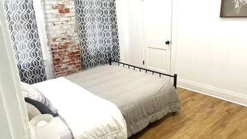 A single bed with a metal frame, a white door, and a patterned curtain.