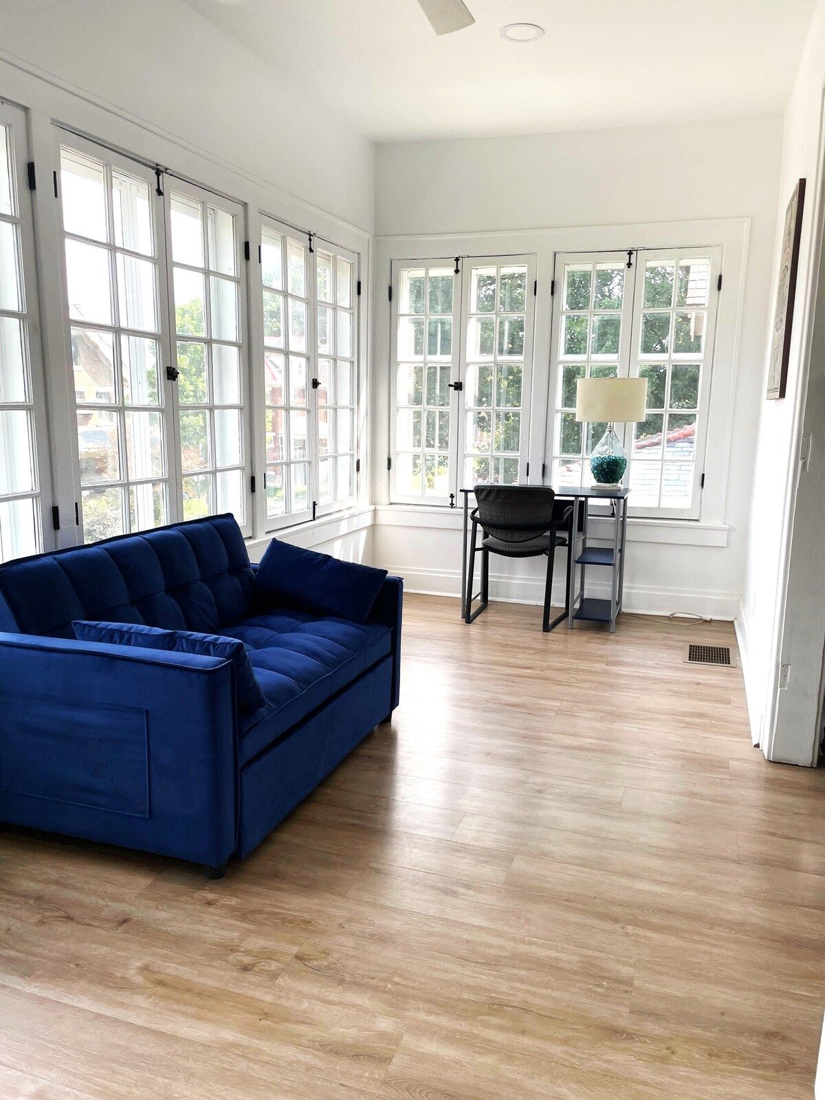 A room with a blue sofa, a chair, a small table with a lamp, and large windows.