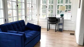 A room with a blue sofa, a chair, a small table with a lamp, and large windows.