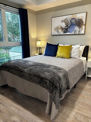 Ein Schlafzimmer mit einem Bett, einem Nachttisch, einer Lampe und einem Fenster mit Vorhängen.
