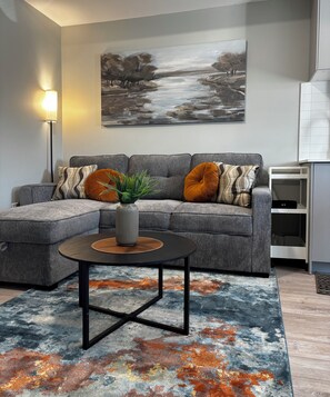 A modern living room with a sectional sofa, a coffee table, and a painting on the wall. - 1 Bedroom Condo/6 minutes from Niagara Falls. (Niagara Falls)