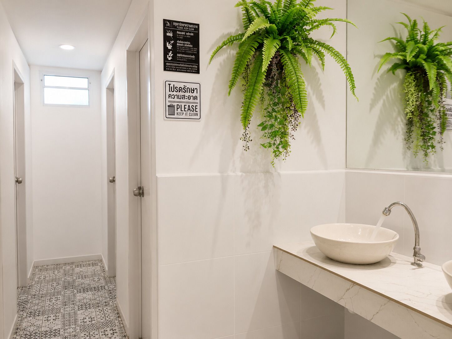 A bathroom with a white sink, a mirror, and a sign that says 'Please keep it clean.' There are hanging plants above the sink.