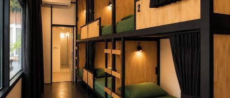 A corridor with bunk beds, numbered room doors, and a view of an outdoor area.