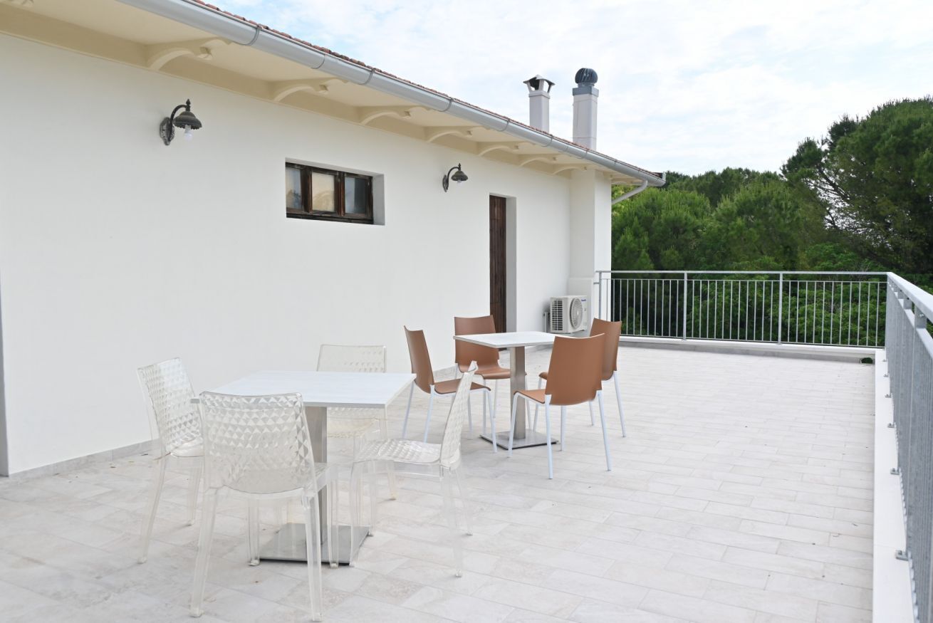 Een terras met een tafel, stoelen, een airconditioning en een balustrade.