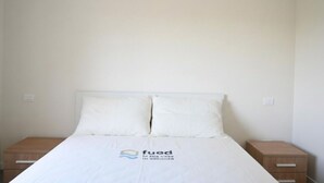 A simple, clean hotel room with a bed, two nightstands, and a logo on the bedspread. - S373 – Sirolo, new one-bedroom apartment with a/c, convenient to the beach (Sirolo)
