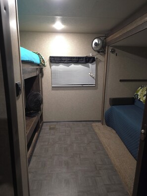 A compact room with bunk beds, a window with blinds, a fan, and a small heater. - Jolly RV: 2 bdrm RV in lovely Spring Branch/Canyon Lake/Hill Country w/AC, grill (Spring Branch)
