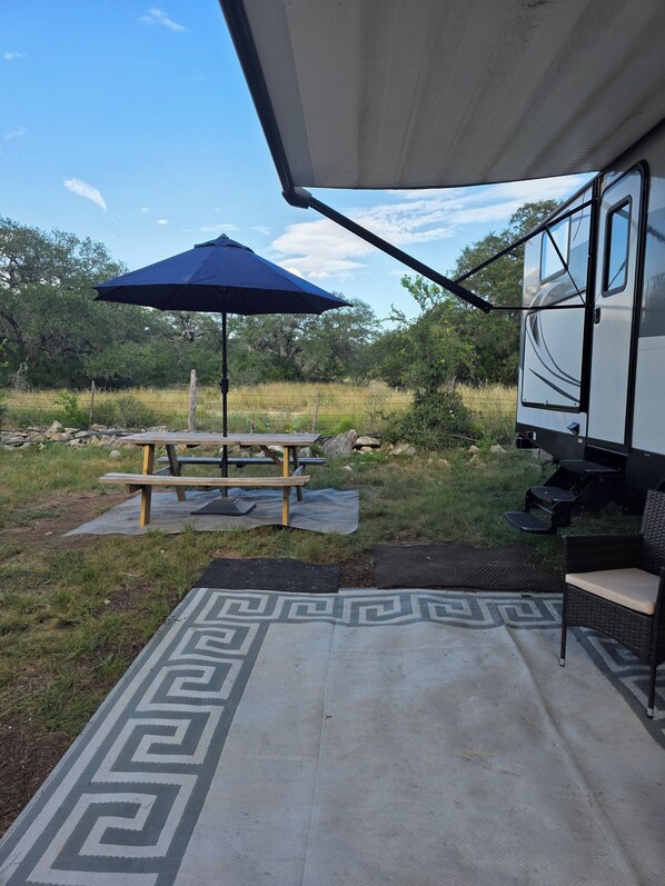 A covered outdoor area with a picnic table, an umbrella, and a grill. - Jolly RV: 2 bdrm RV in lovely Spring Branch/Canyon Lake/Hill Country w/AC, grill (Spring Branch)
