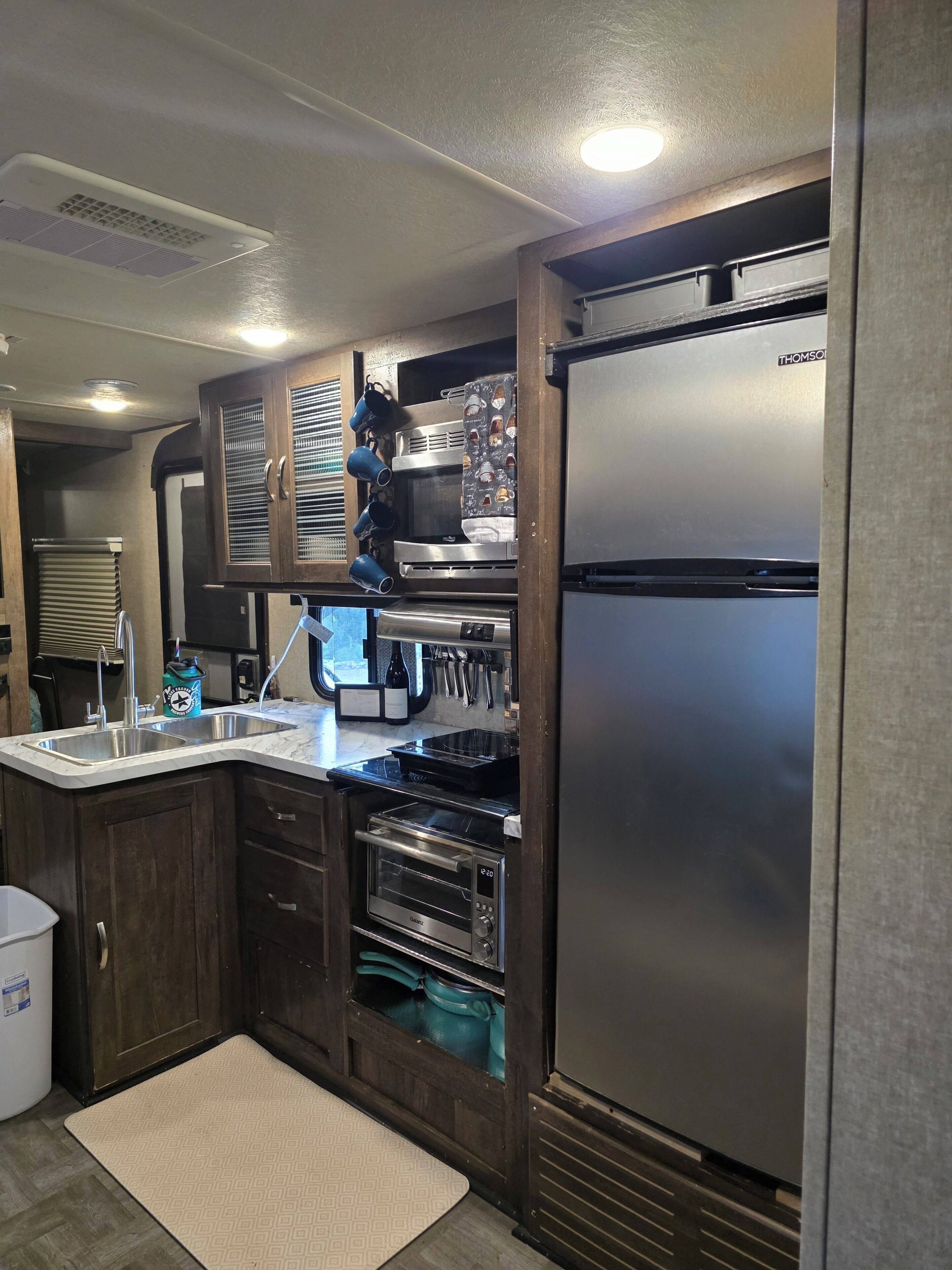 Cocina compacta con refrigerador de acero inoxidable, horno empotrado y microondas.