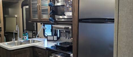 Cocina compacta con refrigerador de acero inoxidable, horno empotrado y microondas.