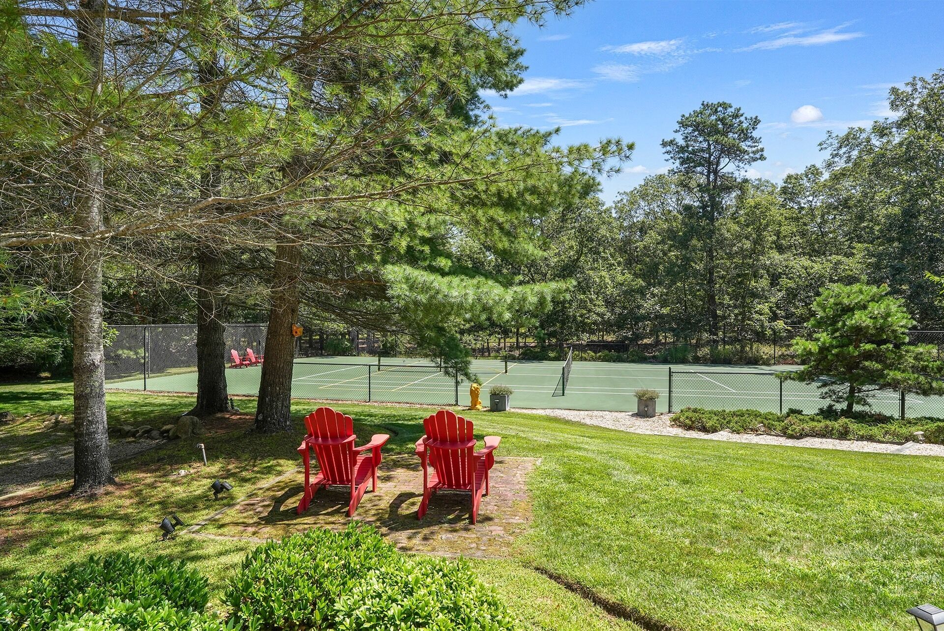 A tennis court with a net, surrounded by trees and grass.