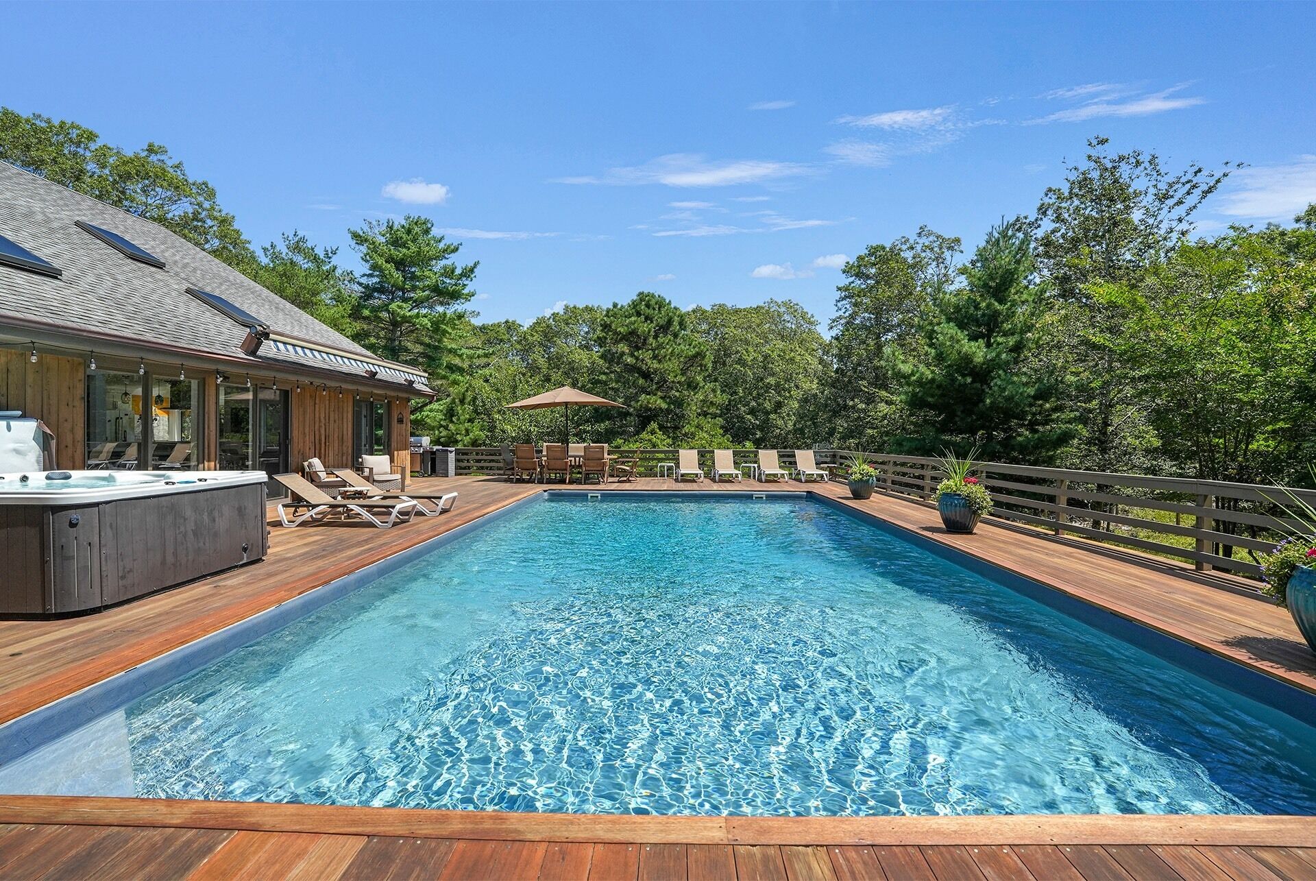 A rectangular swimming pool with a wooden deck, lounge chairs, and a hot tub.